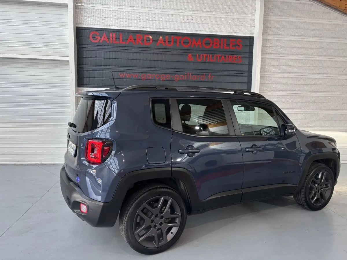 Jeep Renegade bleu en vue 3/4 arrière côté gauche, avec toit noir et jantes foncées dans un garage.