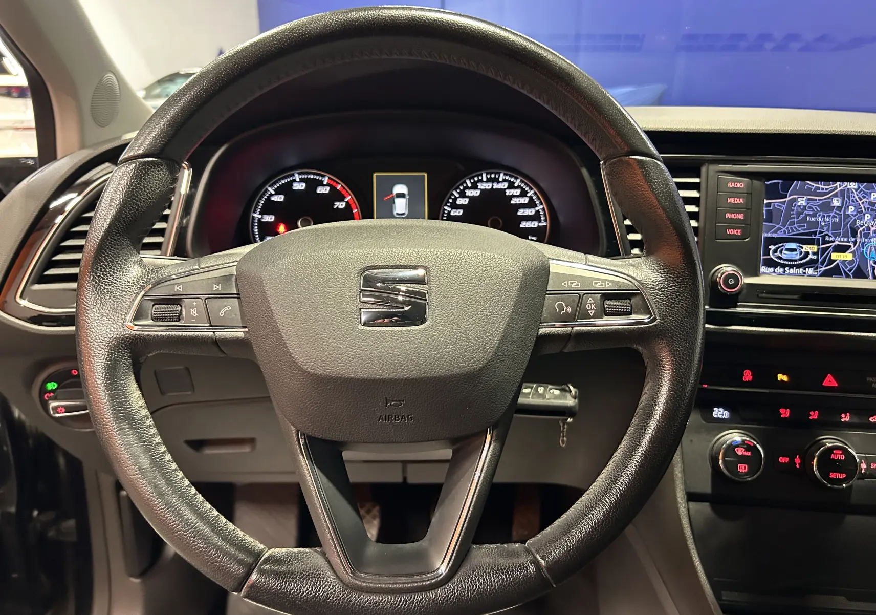 Vue intérieure centrée sur le volant en cuir noir d'une SEAT Leon 2014 avec tableau de bord et écran GPS allumé.