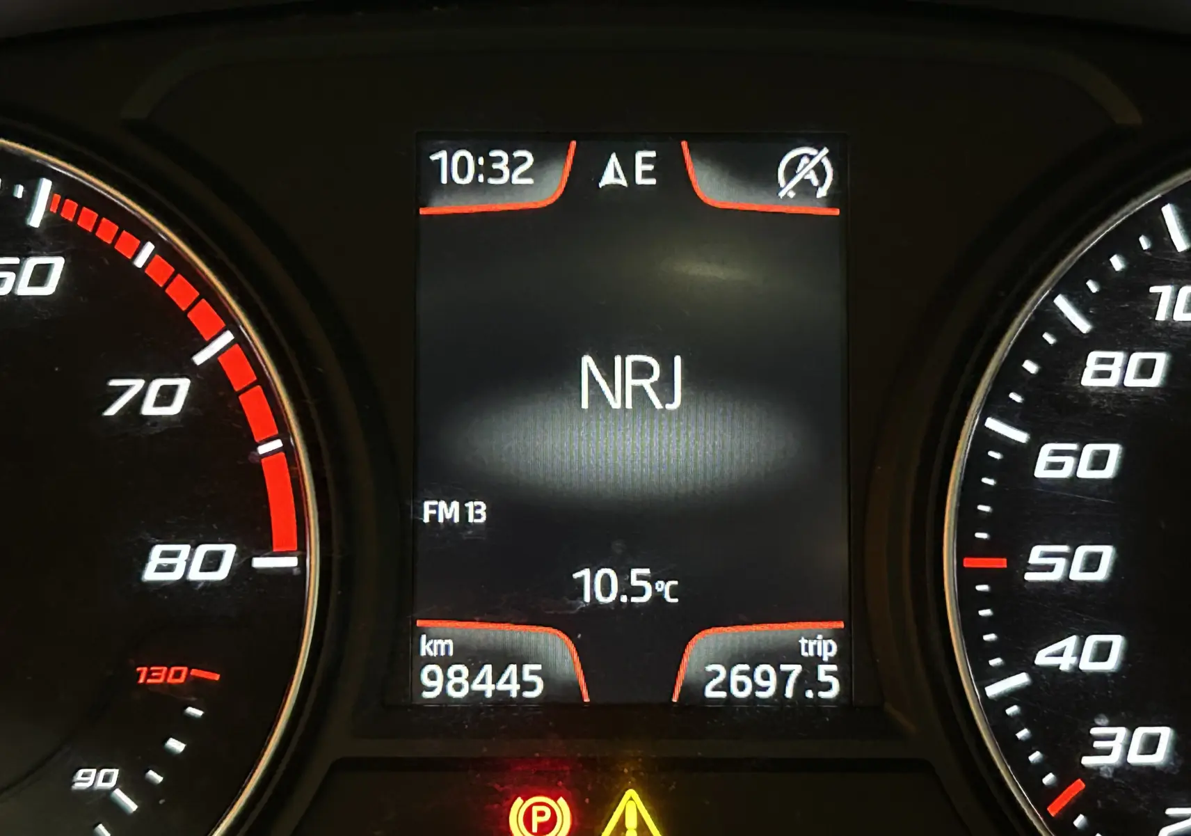 Gros plan sur le tableau de bord numérique d'une SEAT Leon 2014, affichant la radio NRJ et le compteur kilométrique.