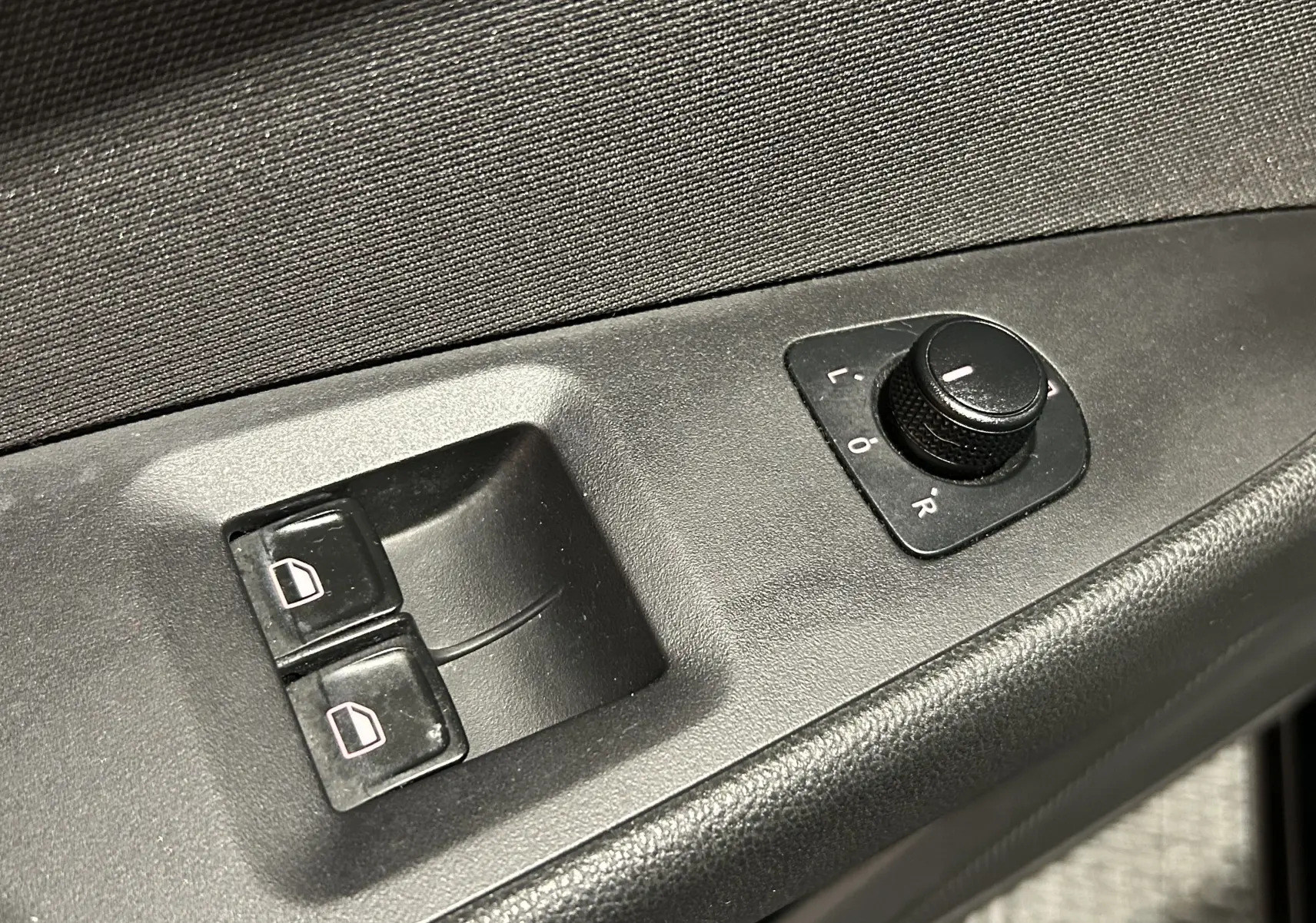 Gros plan sur les commandes de réglage des rétroviseurs et des vitres électriques côté conducteur d’une SEAT LEON noire.