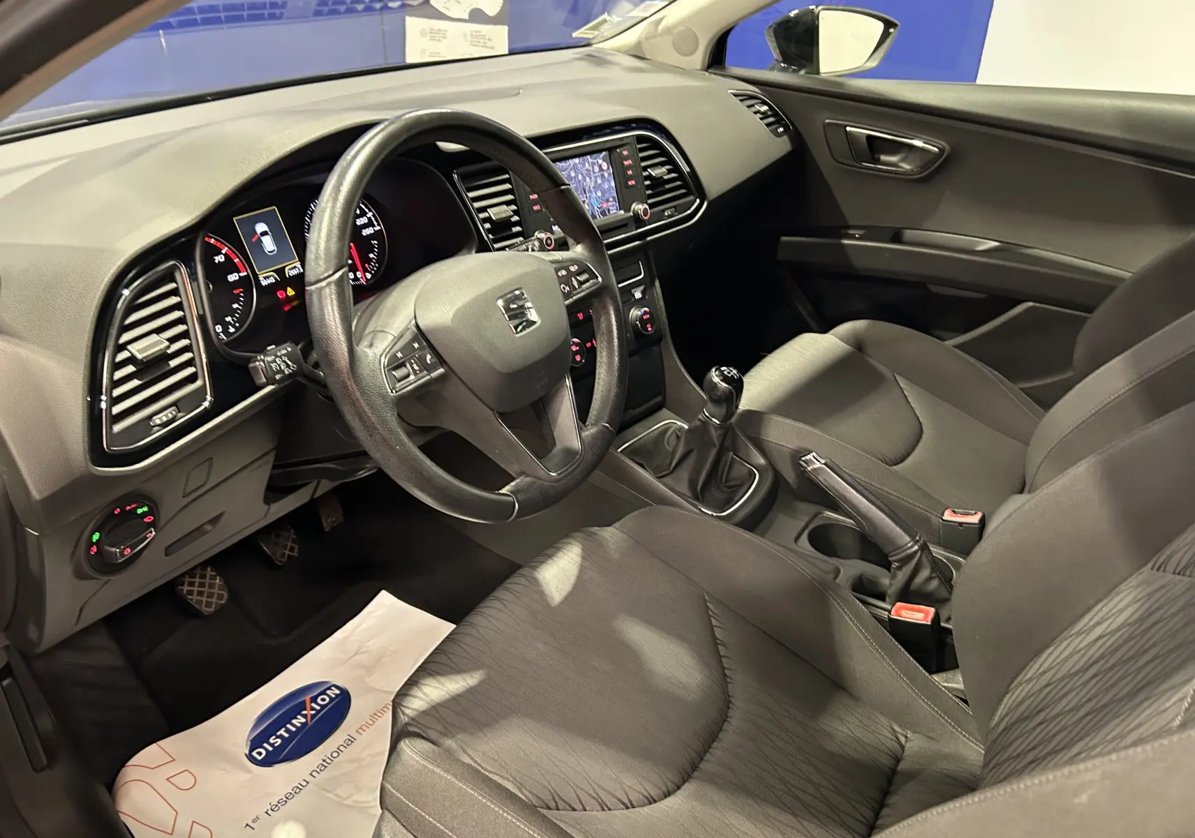 Vue intérieure côté conducteur de la SEAT Leon noire, montrant le volant cuir, la boîte manuelle et l’écran GPS intégré.