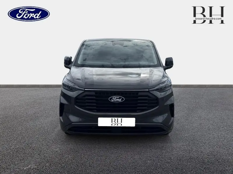 Vue frontale du Ford Transit Custom Fourgon 2026 en gris Magnetic métallisé avec calandre noire et phares LED intégrés.