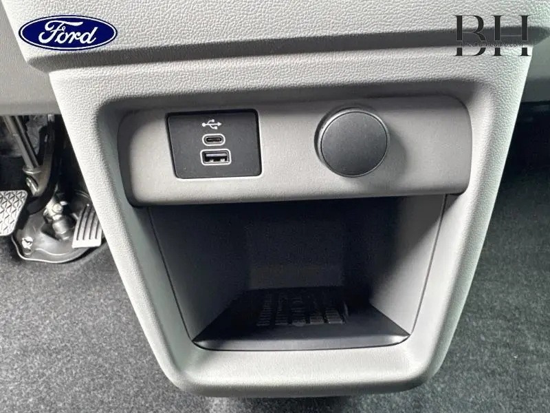 Gros plan sur le bac de rangement gris du Ford Transit Custom Fourgon avec prise USB et prise 12V, intérieur noir.