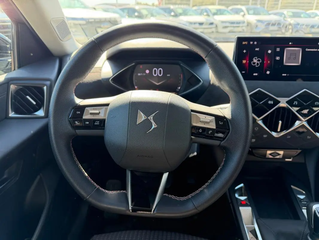 Vue intérieure centrée sur le volant du DS3 2024 gris, avec tableau de bord numérique et commandes intégrées au volant.