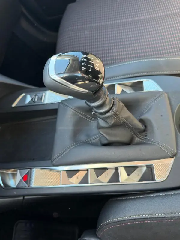 Gros plan sur le levier de vitesse manuel noir du DS3 100 BVM6 Performance Line 2024, avec console centrale en cuir gris et boutons argentés.