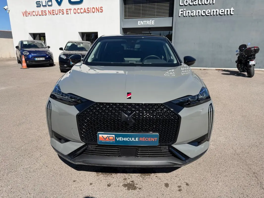Vue frontale d’une DS3 100 BVM6 Performance Line gris 2024 avec calandre noire et phares étirés, en extérieur devant un concessionnaire.