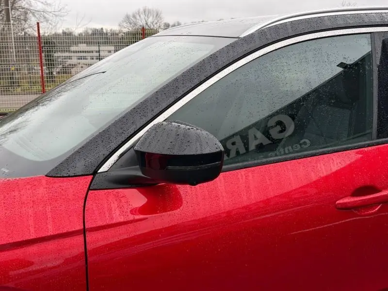 Vue latérale côté gauche du Renault Austral 2025 rouge flamme, mettant en valeur la porte et le rétroviseur noir sous la pluie.