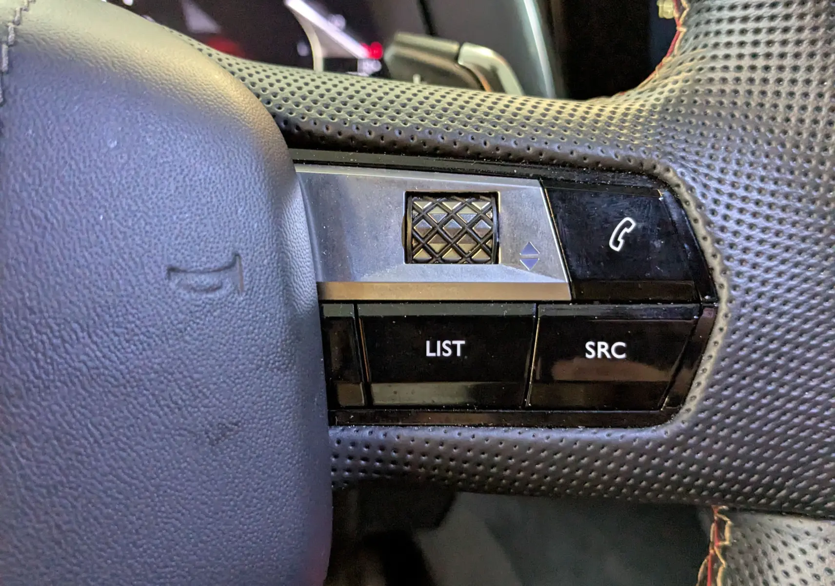 Gros plan sur les commandes gauche du volant perforé noir du DS7 2025, avec molette et boutons LIST et SRC.