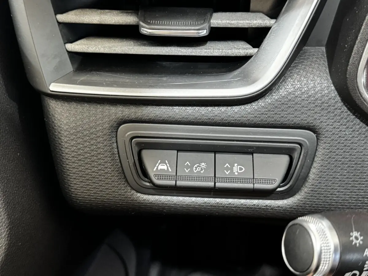 Gros plan sur les boutons de réglage des aides à la conduite et des phares dans une Renault Clio Business gris clair, côté gauche.