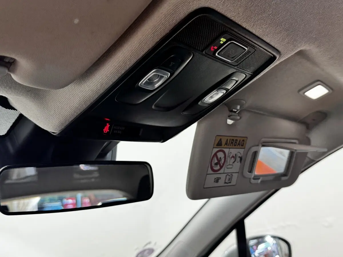 Détail intérieur du plafond avant de la Renault Clio gris clair, avec miroir de soleil ouvert et commandes d’éclairage.