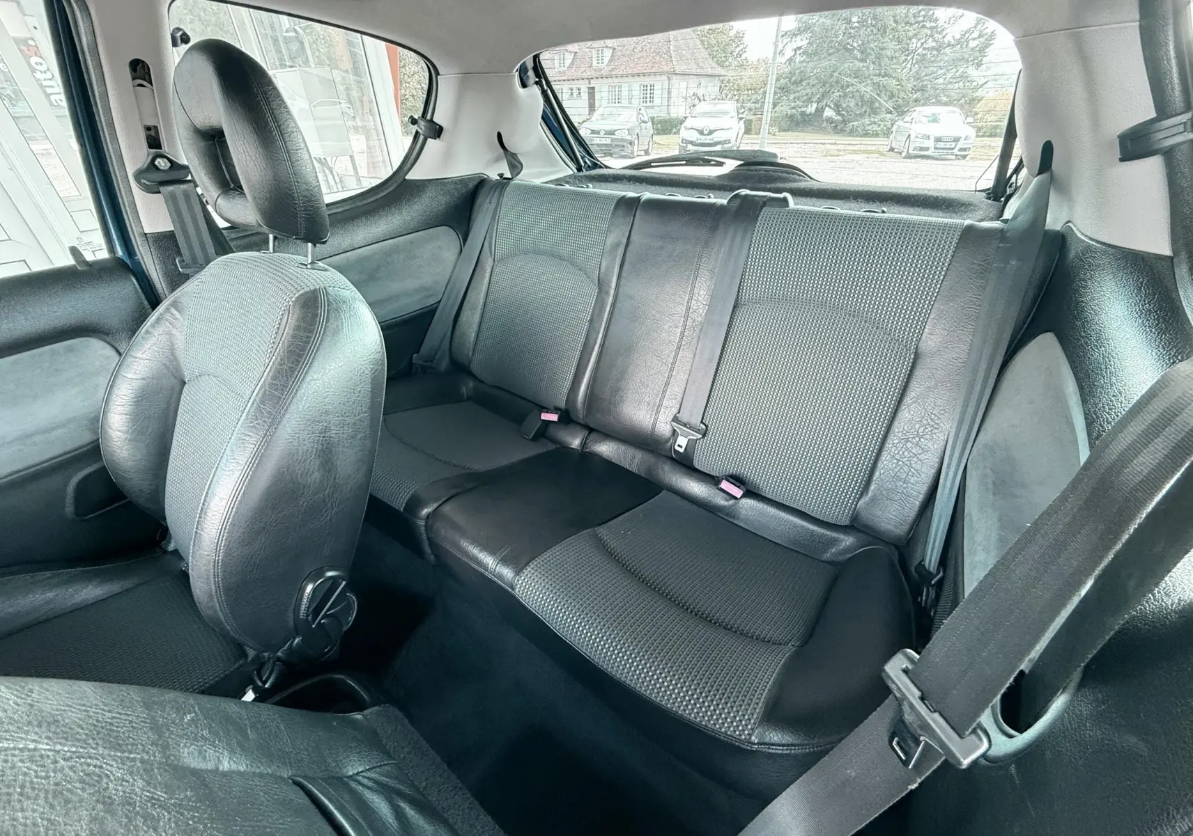 Vue intérieure arrière de la Peugeot 206 bleu, montrant les sièges arrière en cuir et tissu noir avec ceintures de sécurité.