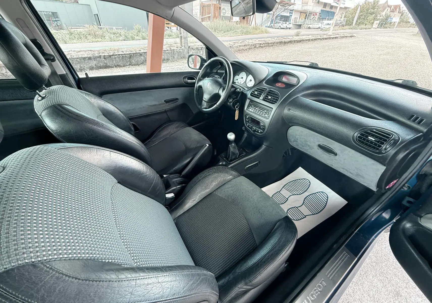 Vue intérieure côté conducteur de la Peugeot 206 16v 2L 136CH 2003 avec sièges cuir et tissu noirs.