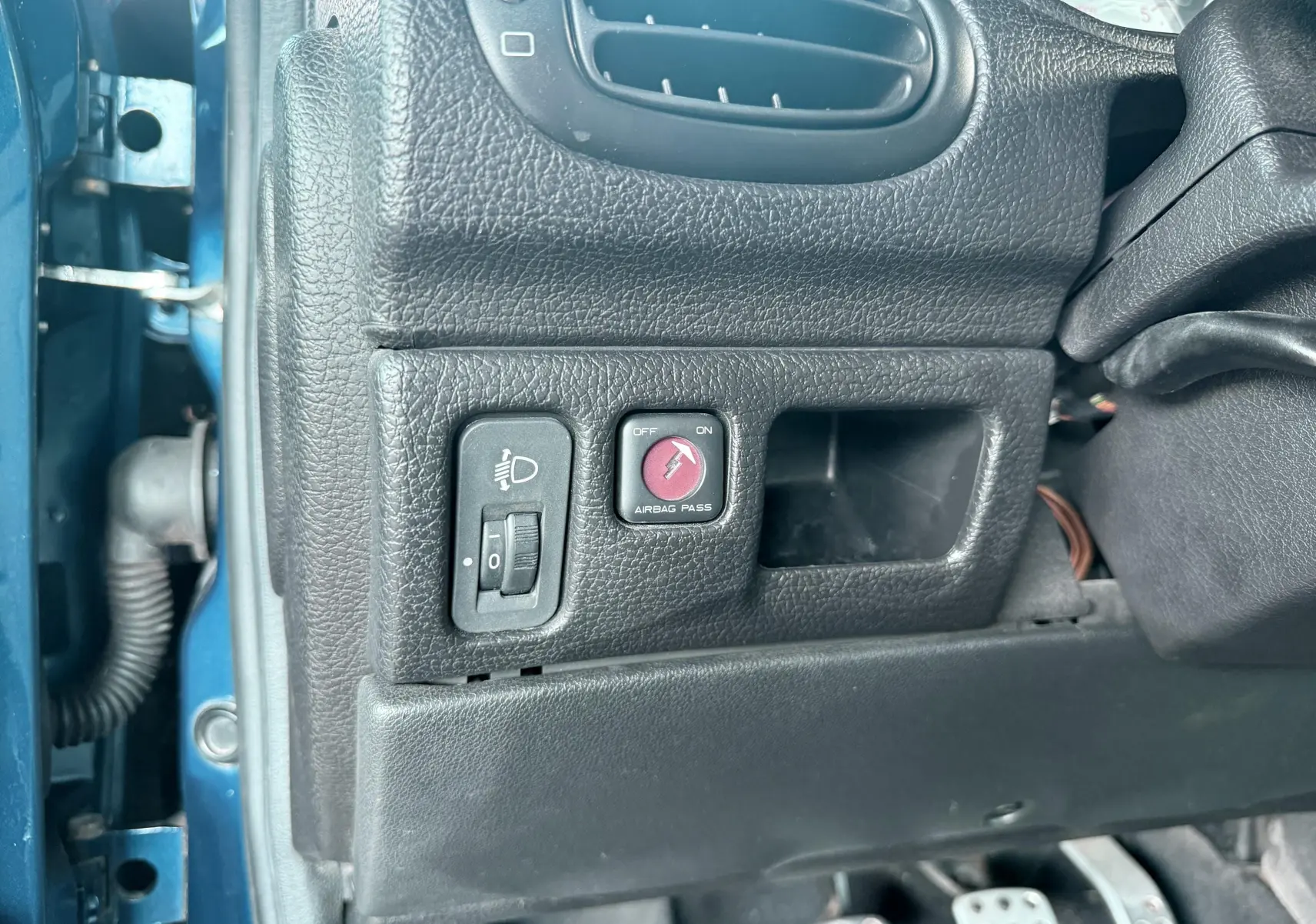Détail intérieur côté gauche d’un Peugeot 206 bleu, montrant les commandes de réglage des phares et désactivation de l’airbag passager.