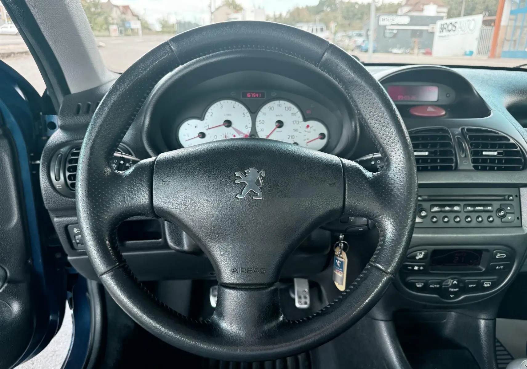 Vue intérieure centrée sur le volant en cuir noir de la Peugeot 206 bleu, avec tableau de bord et commandes visibles.