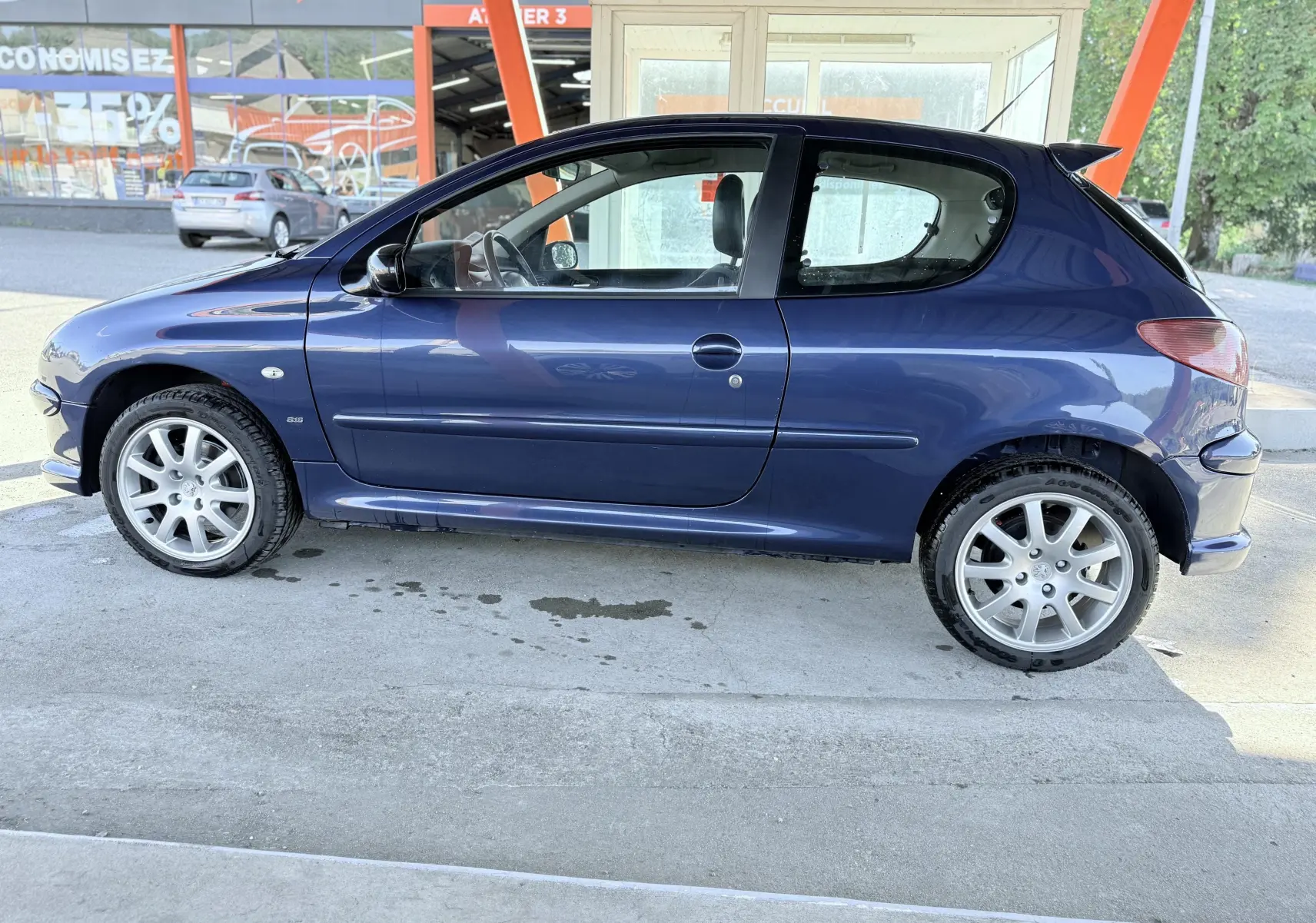 Peugeot 206 bleu en vue profil côté gauche, avec jantes alliage et toit arrière légèrement surélevé.
