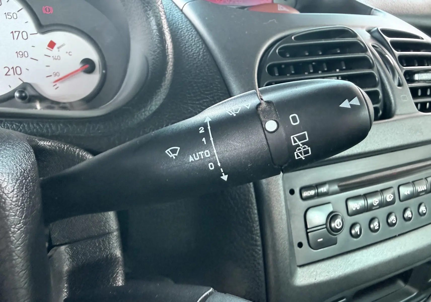 Gros plan sur la commande d’essuie-glace côté gauche du tableau de bord noir d’une Peugeot 206 bleue de 2003.