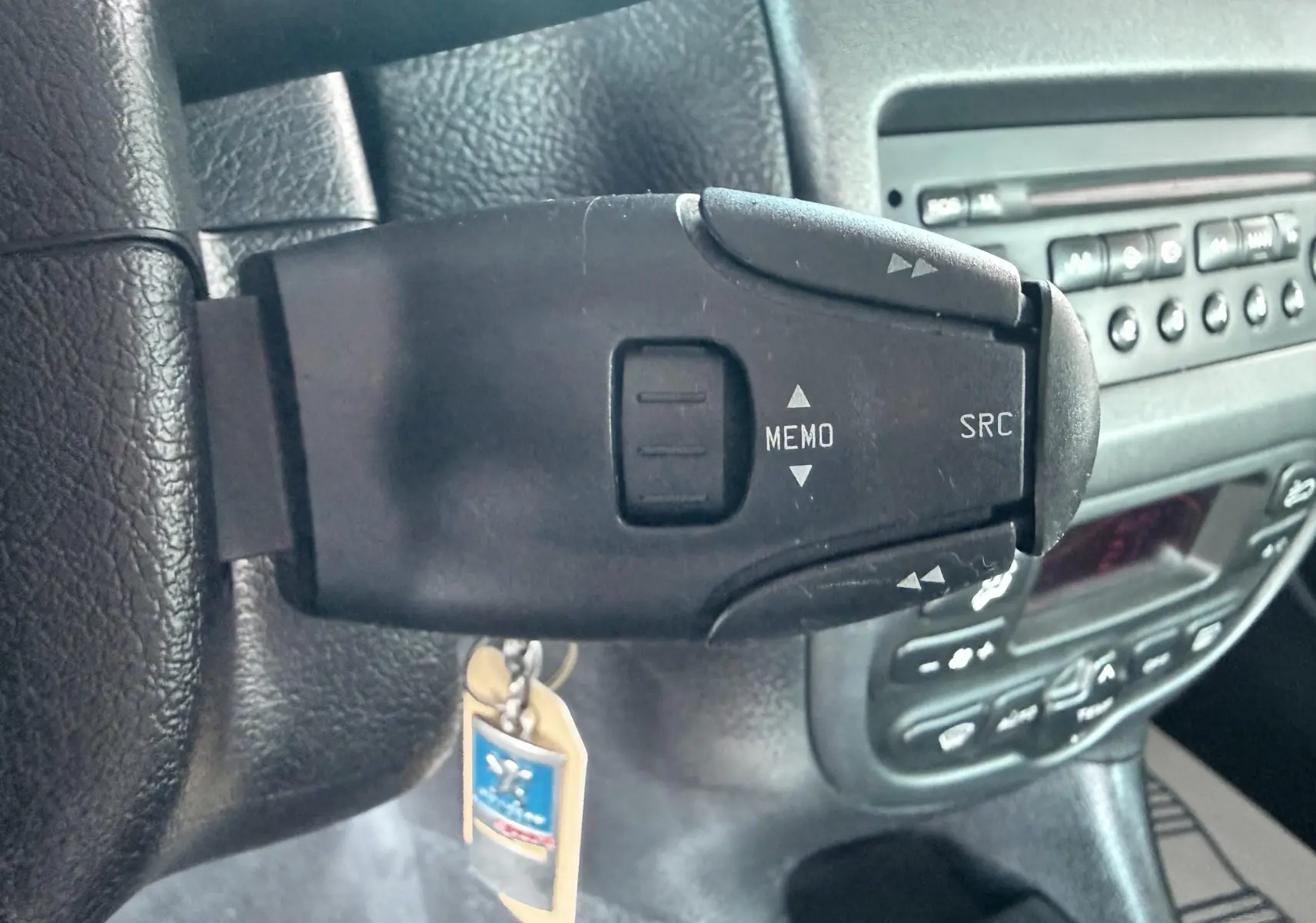 Gros plan sur la commande au volant gauche d’une Peugeot 206, avec tableau de bord et autoradio en arrière-plan.
