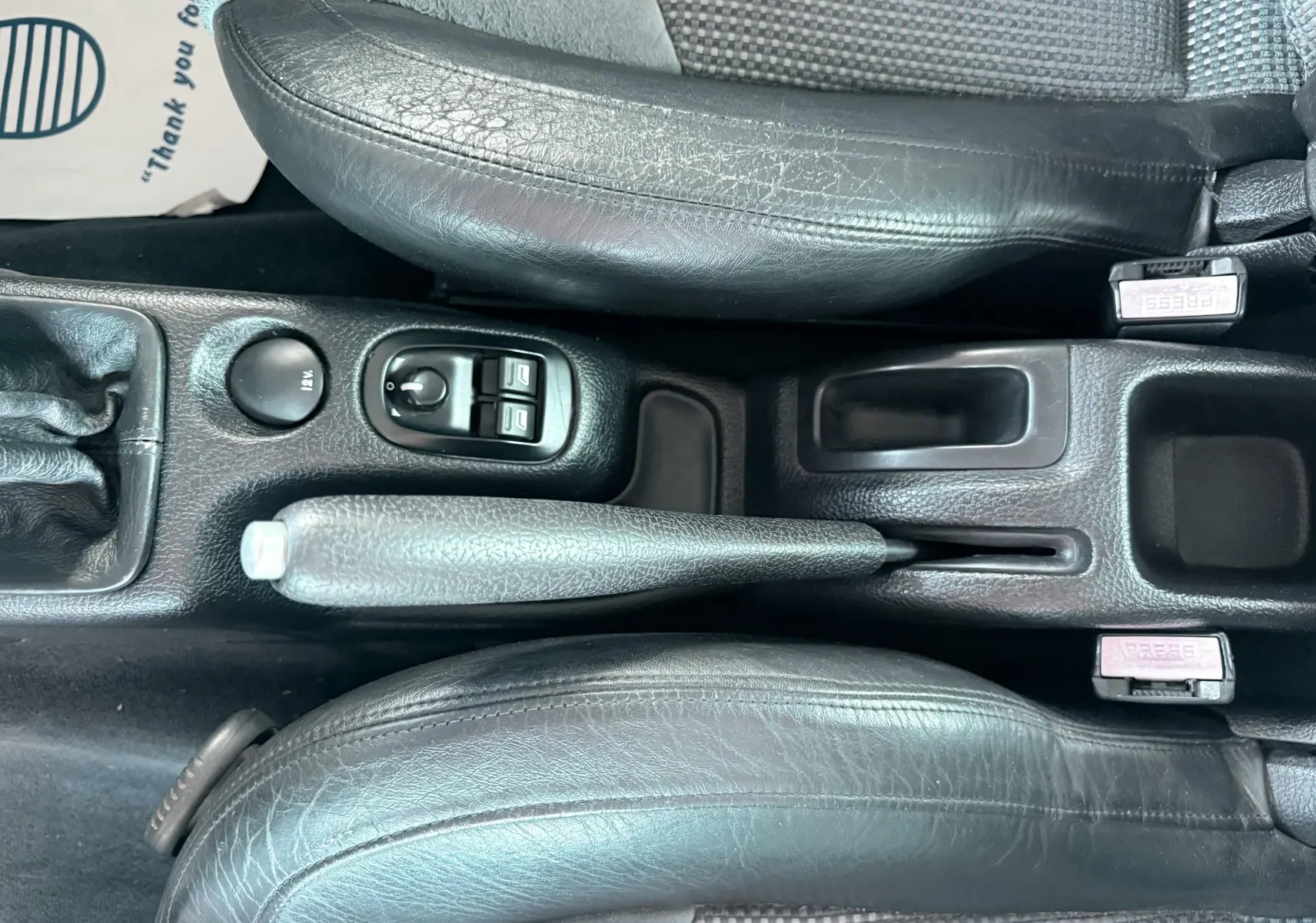 Vue plongeante sur la console centrale noire en cuir et tissu du Peugeot 206 16v 2L avec frein à main et commandes électriques.