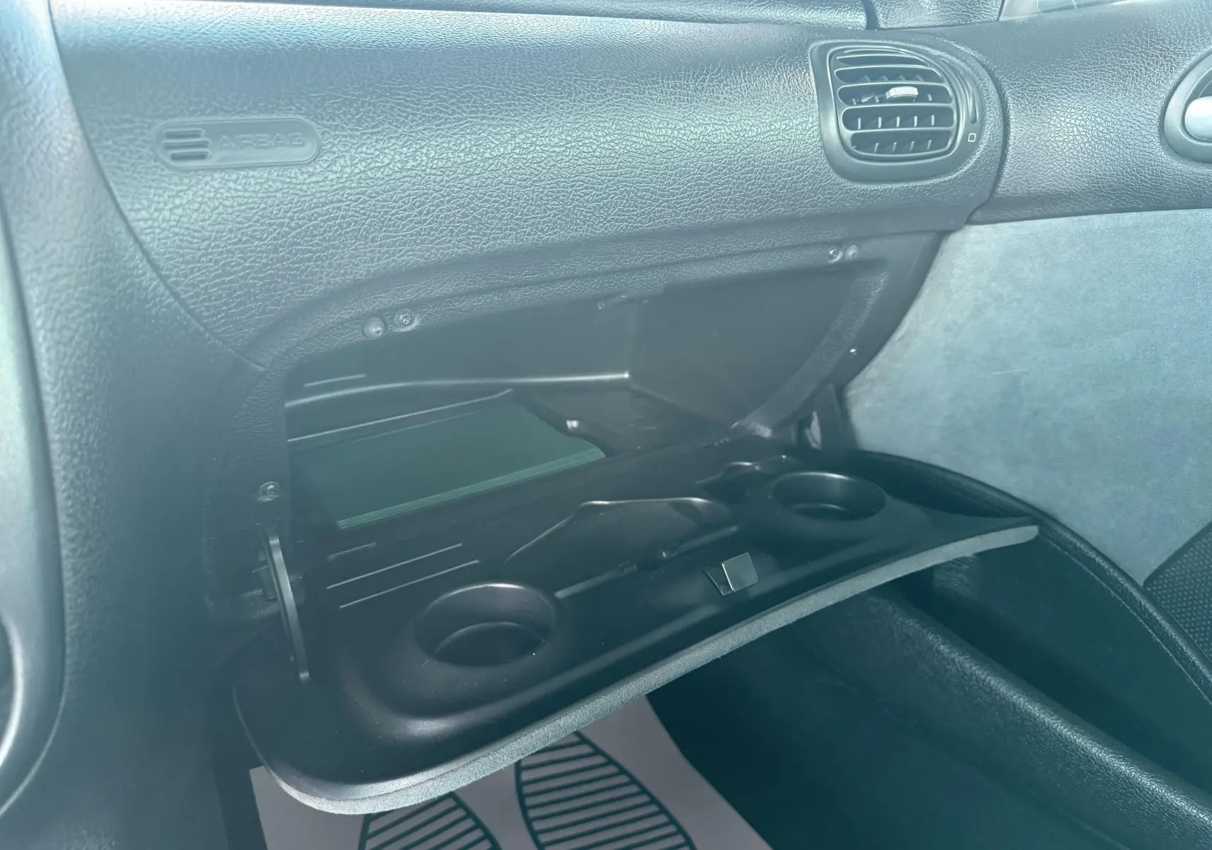 Intérieur de la Peugeot 206 bleu de 2003, vue rapprochée de la boîte à gants ouverte avec porte-gobelets intégrés.