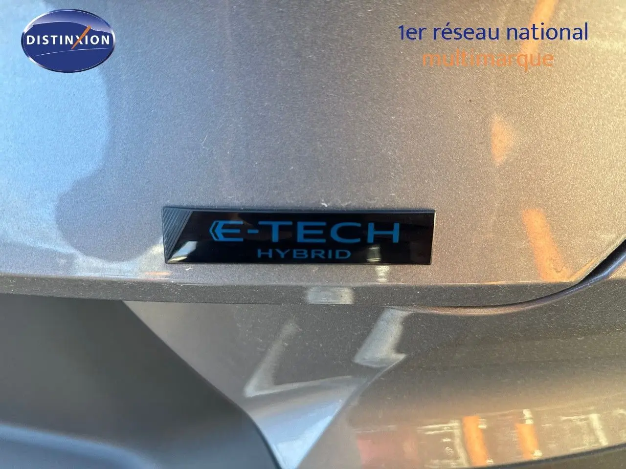 Gros plan sur l'insigne E-TECH Hybrid sur la carrosserie gris cassiopée métal d'une Renault Symbioz 2024.