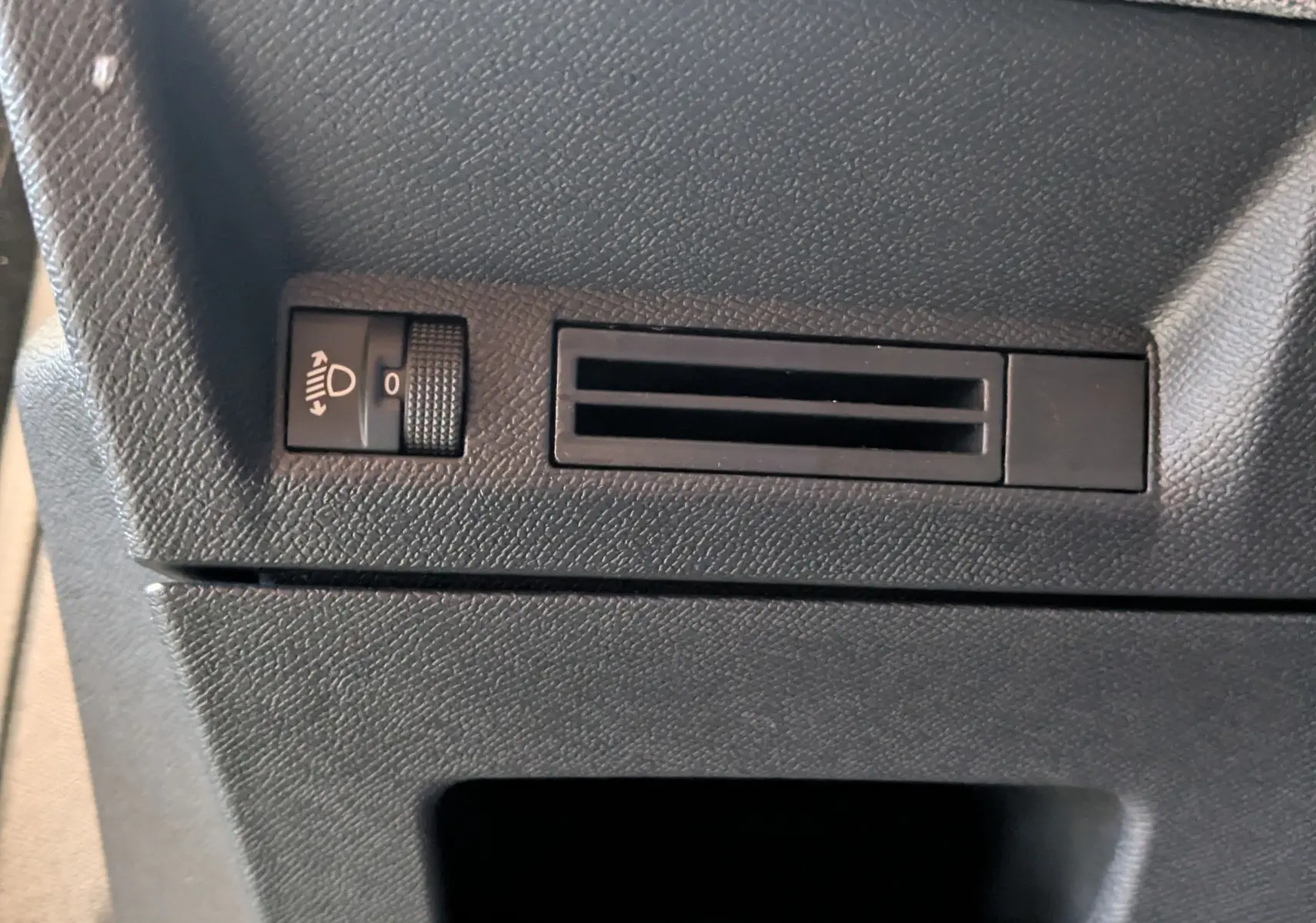 Détail du tableau de bord noir du Peugeot 3008 Hybrid 145, avec réglage de hauteur des phares et prise d'air.