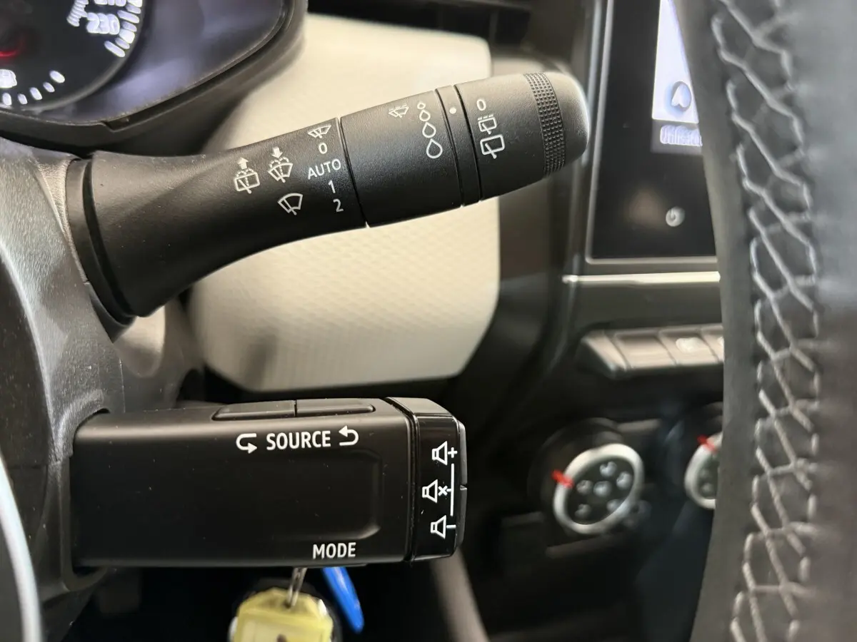 Gros plan sur les commandes des essuie-glaces et multimédia à gauche du volant d’une Renault Clio blanche 2023.