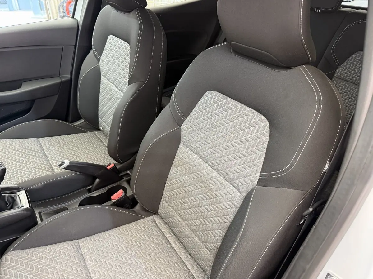 Vue rapprochée des sièges avant gris et noirs de la Renault Clio Evolution TCe 100 GPL 2023, avec volant et levier de vitesse visibles.