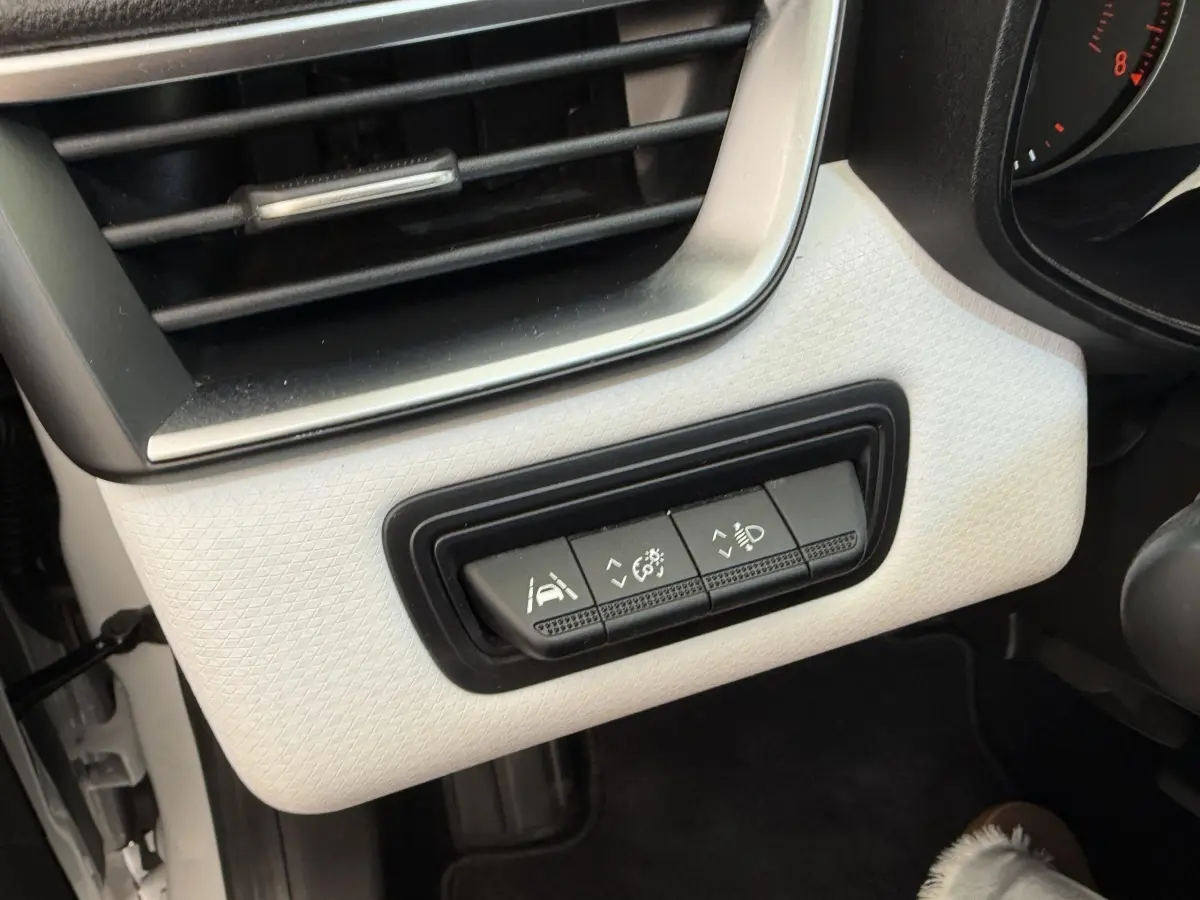 Gros plan sur les commandes d'assistance et éclairage sur tableau de bord blanc côté conducteur d'une Renault Clio 2023.