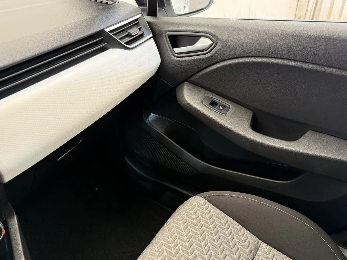 Intérieur côté passager de la Renault Clio blanc, montrant la porte noire et la partie basse du tableau de bord blanc.