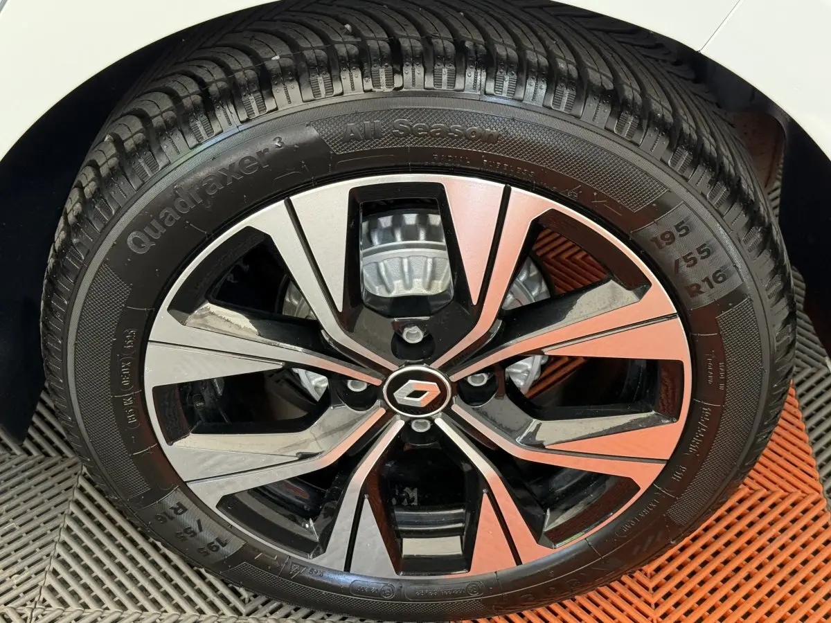 Gros plan sur la roue avant droite d’une Renault Clio blanche, jante alliage bicolore au design moderne.