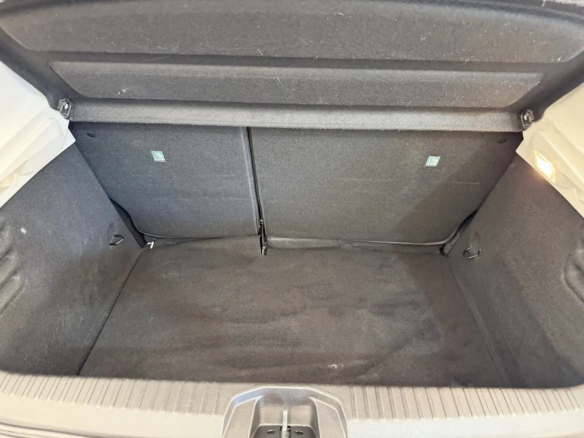 Vue intérieure du coffre ouvert d'une Renault Clio blanche 2023, montrant un espace de rangement propre et tapissé en tissu noir.