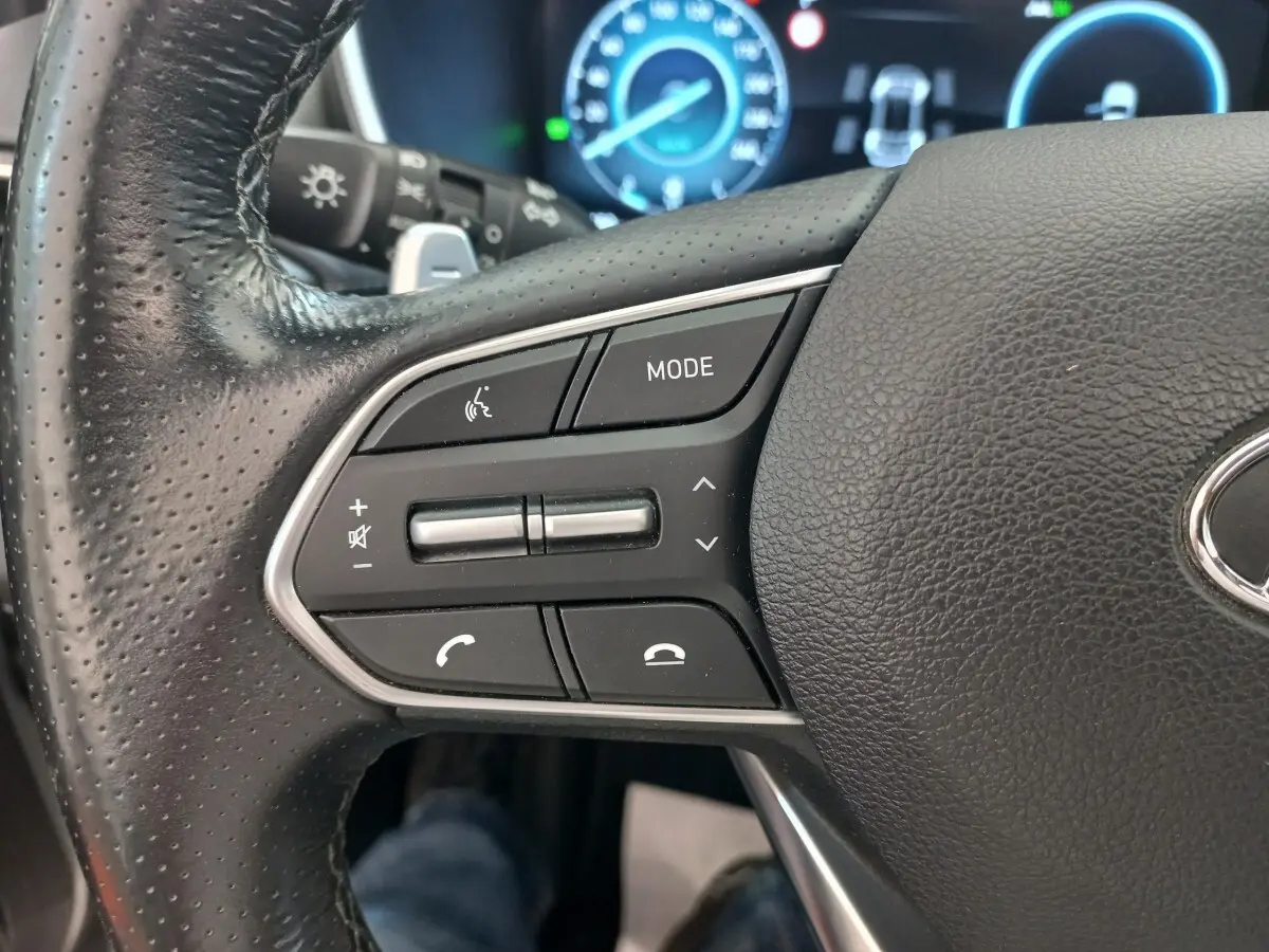 Gros plan sur le volant cuir noir du Hyundai Santa Fe 2022, avec commandes multifonctions et tableau de bord numérique bleu.