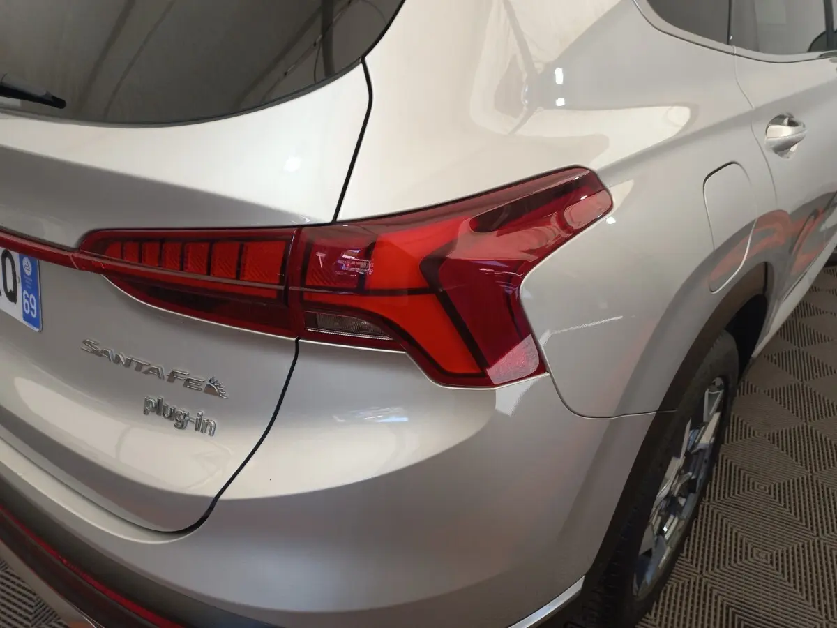 Vue 3/4 arrière droite d’un Hyundai Santa Fe gris clair avec feux arrière LED et badge plug-in visible.