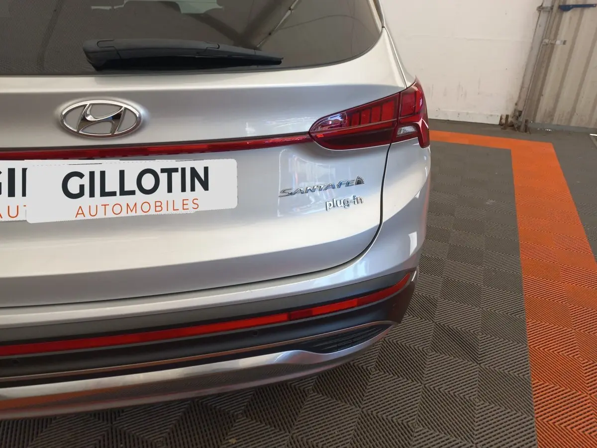 Vue arrière droite du Hyundai Santa Fe gris clair avec logo et badge plug-in visible sur un sol à motifs gris et orange.