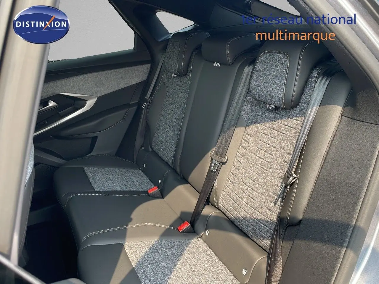 Vue intérieure arrière du Peugeot 3008 Hybrid 2025 montrant les sièges bicolores en cuir noir et tissu gris avec ceintures de sécurité.