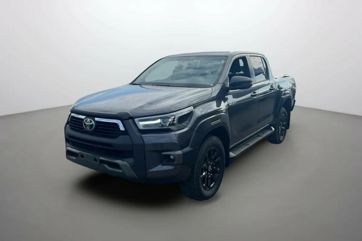 Toyota Hilux 2025 gris atlas en 3/4 avant droit, avec calandre noire et jantes alliage sombres.
