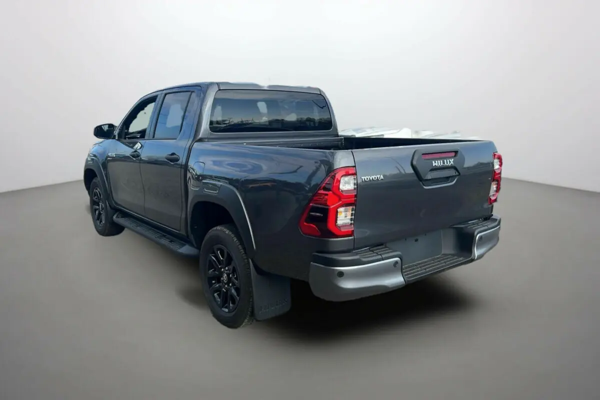 Toyota Hilux 4x4 gris atlas 2025 en vue 3/4 arrière gauche, avec benne ouverte et jantes noires distinctives