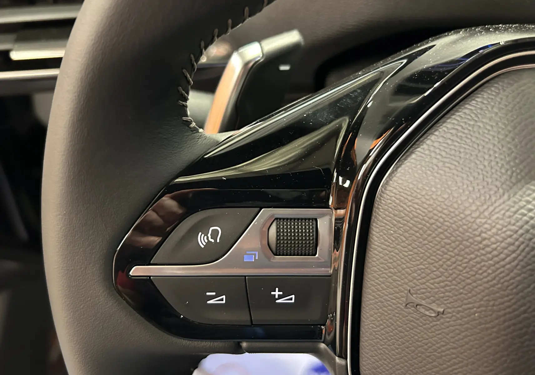 Gros plan sur les commandes du volant noir du Peugeot 5008 2024 finition Allure Pack Gris Platinium.