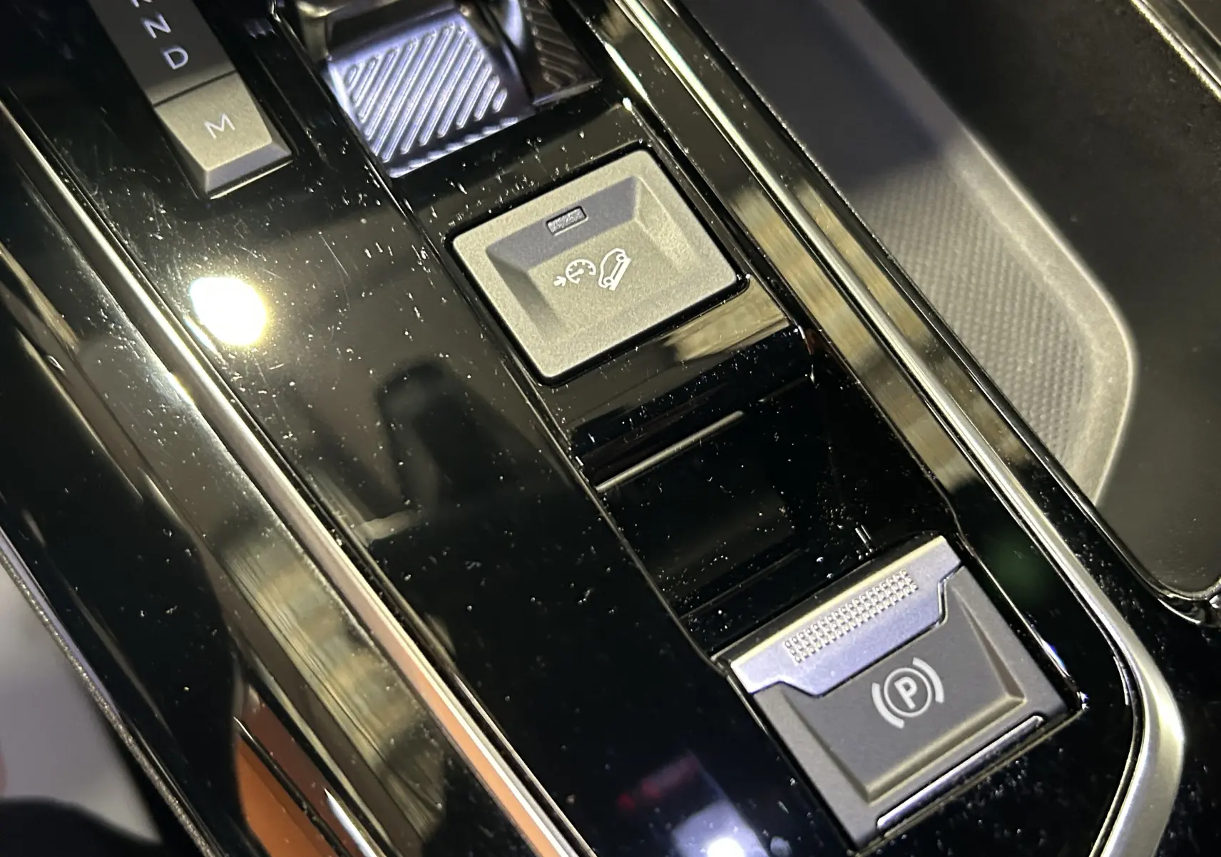 Gros plan sur la console centrale noire brillante du Peugeot 5008 2024 avec commandes de boîte auto et frein électrique.
