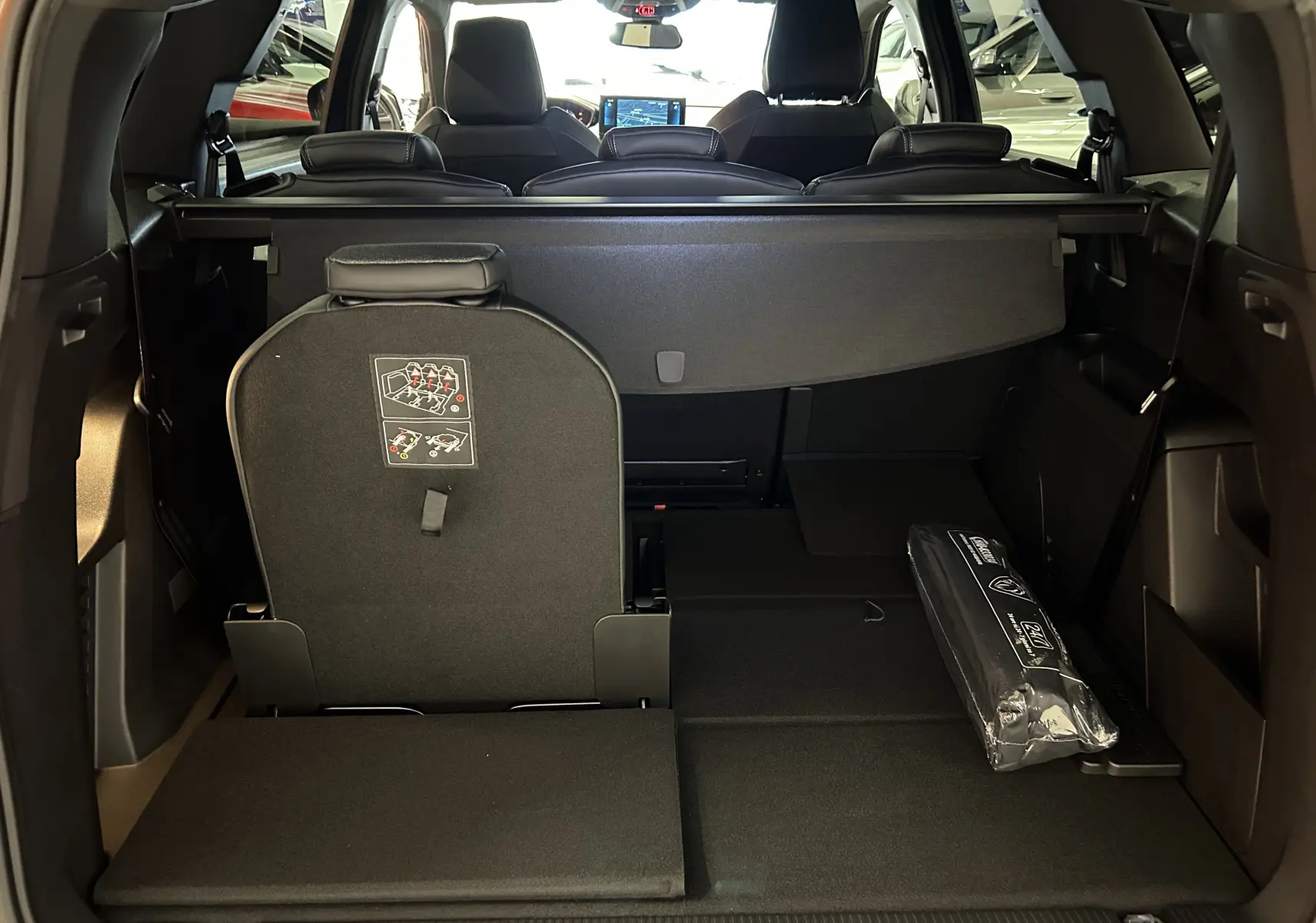 Vue arrière du coffre du Peugeot 5008 gris Platinium 2024, sièges arrière partiellement rabattus et cache-bagages déployé.