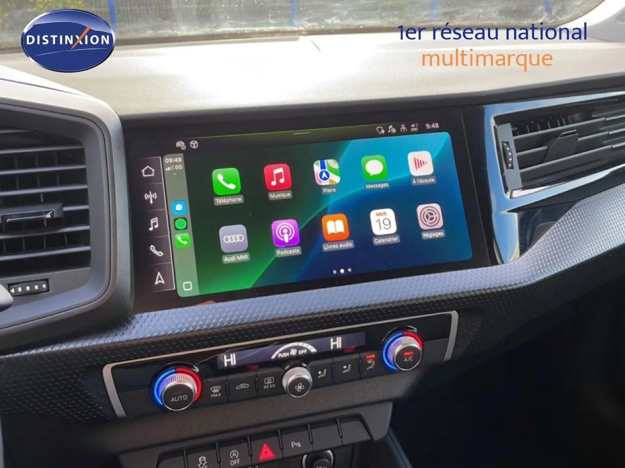 Coffre ouvert d'une Audi A1 Sportback blanc glacier métal, vue arrière montrant l'espace de chargement vide avec tapis noirs.