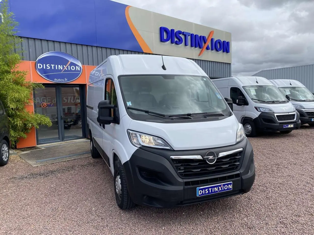Vue 3/4 avant d’un Opel Movano blanc stationné devant un bâtiment avec logo Distinxion.
