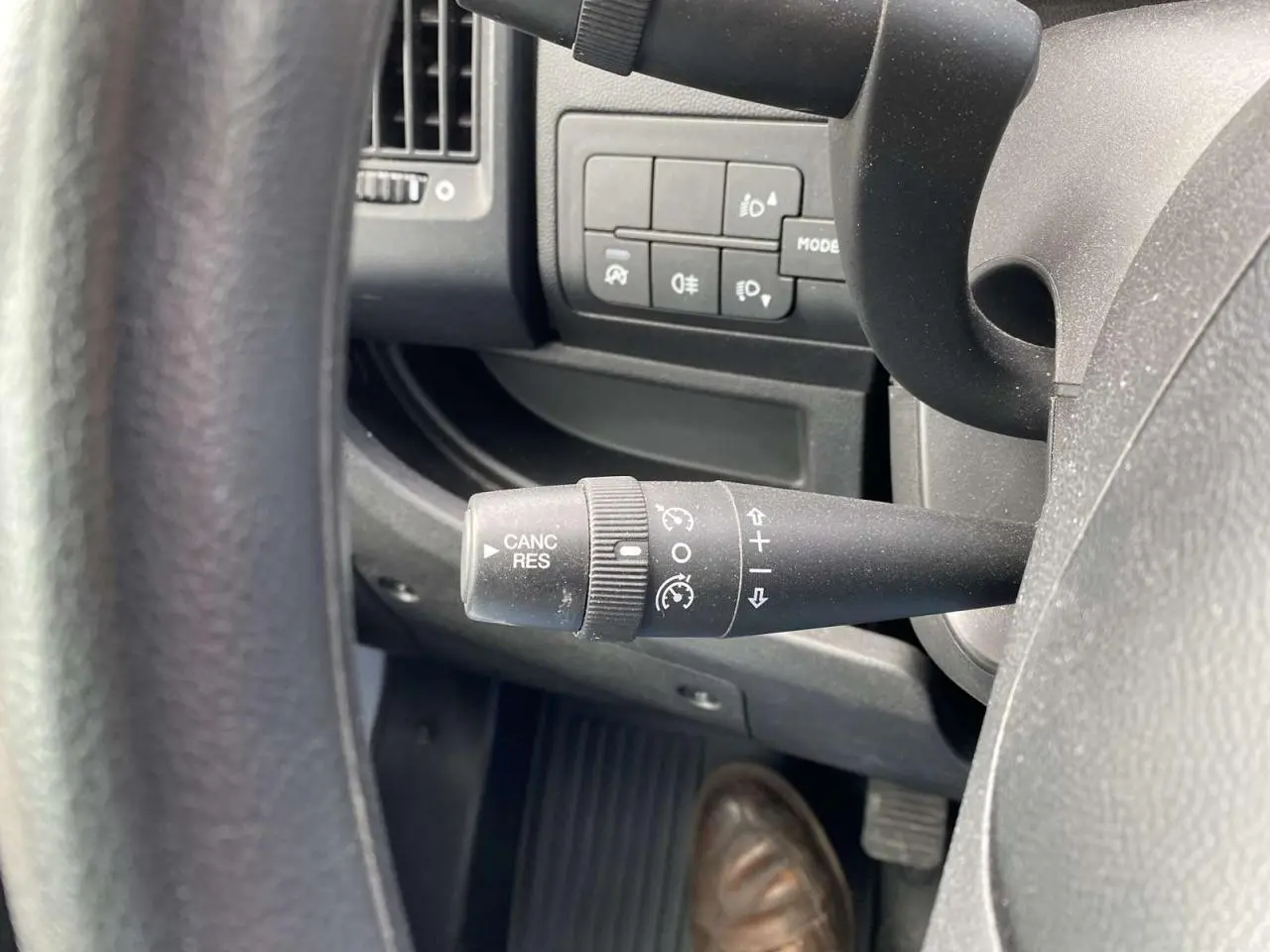Gros plan sur la commande de régulateur de vitesse à gauche du volant dans l'habitacle noir de l'Opel Movano blanc.