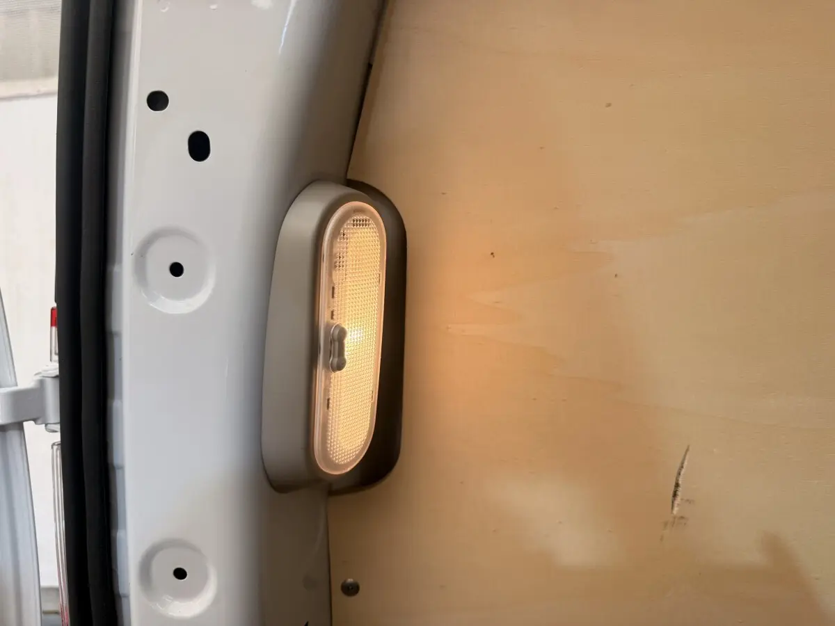 Gros plan sur l’éclairage intérieur blanc allumé dans la zone de chargement d’un Renault Kangoo blanc, cloison bois visible.