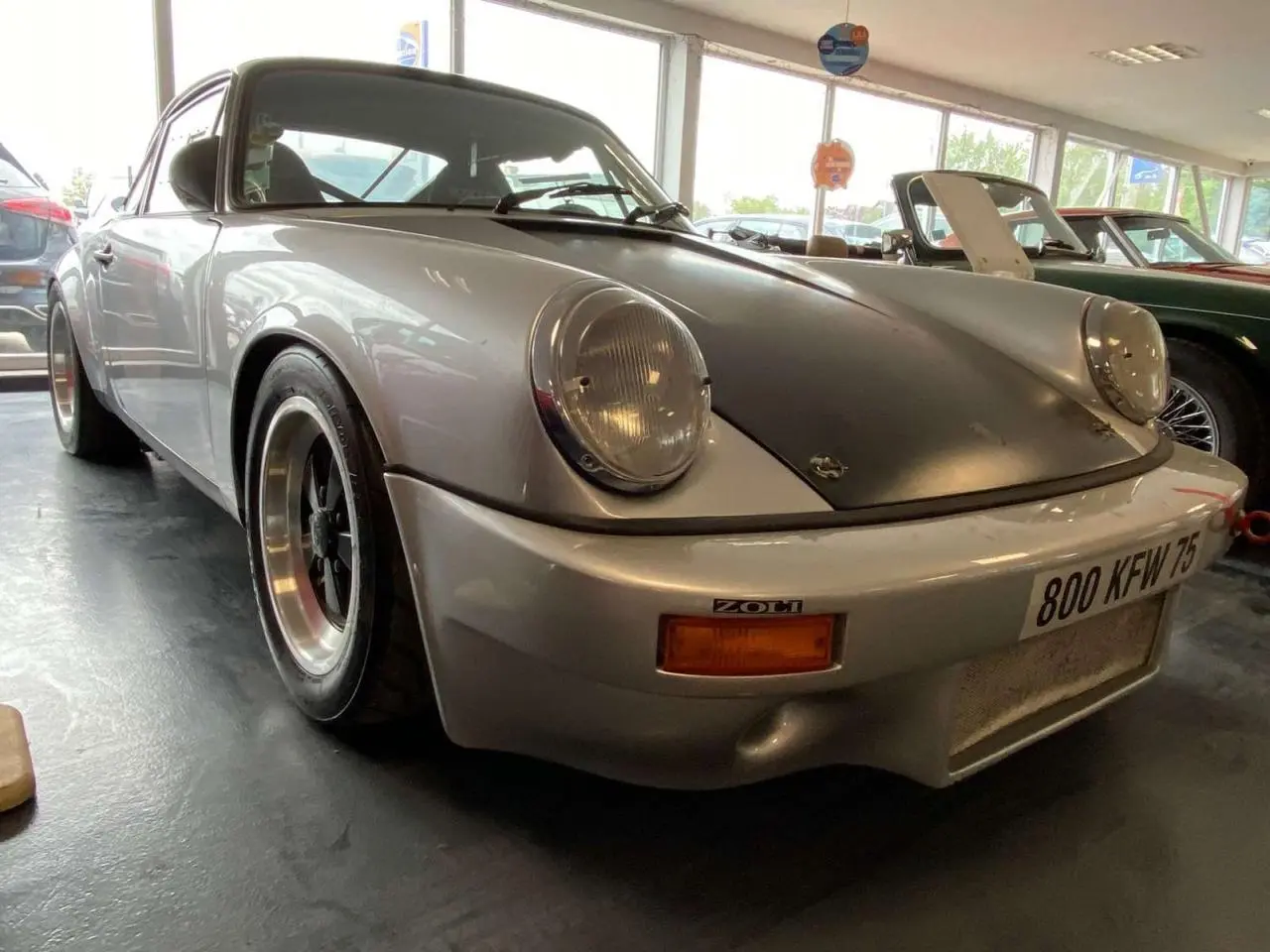 Porsche 911 3.0 SC gris métallisé vue 3/4 avant avec capot noir mat et jantes alliage Fuchs.