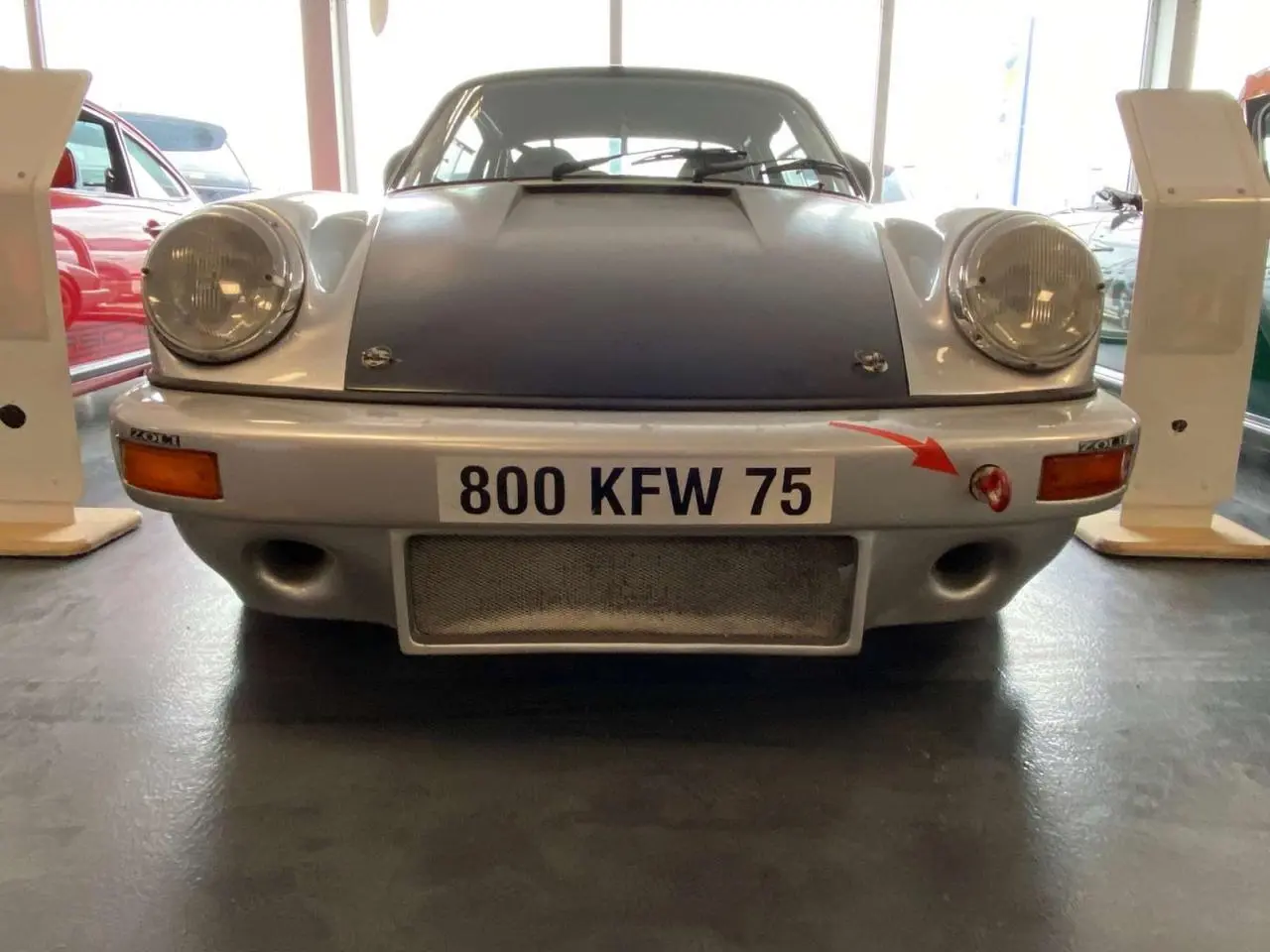 Vue frontale d'une Porsche 911 3.0 SC gris métallisé avec capot noir mat et attache rouge sur pare-chocs.