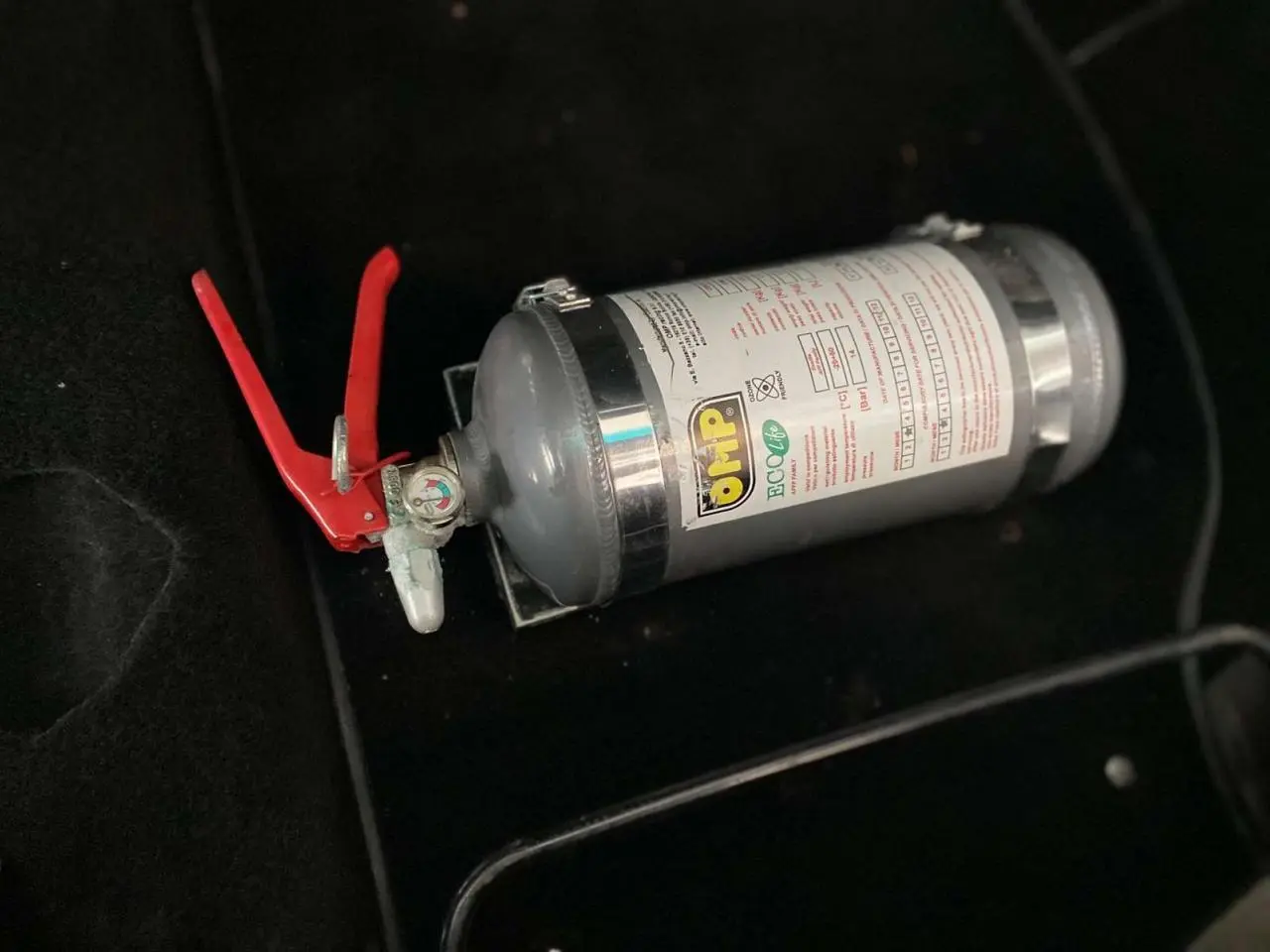 Extincteur OMP gris avec poignée rouge posé sur le sol noir intérieur d'une Porsche 911 3.0 SC 1980.
