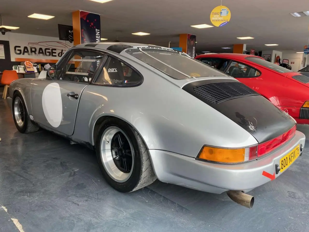 Vue 3/4 arrière droite d'une Porsche 911 3.0 SC 930 gris métallisé avec jantes Fuchs et vitre arrière Lexan en intérieur de garage.