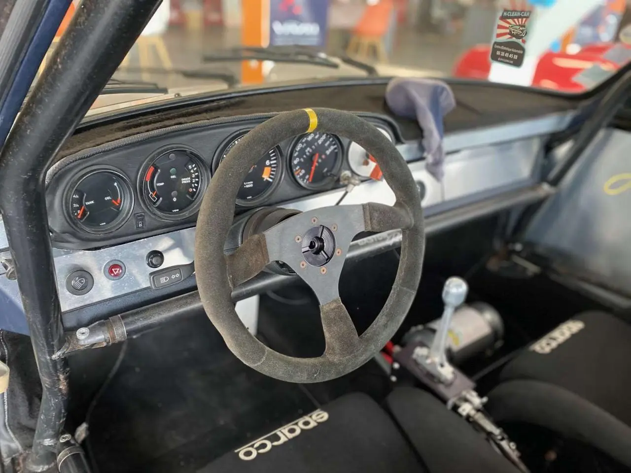 Vue intérieure côté conducteur du tableau de bord aluminium et volant Sparco d’une Porsche 911 3.0 SC course.