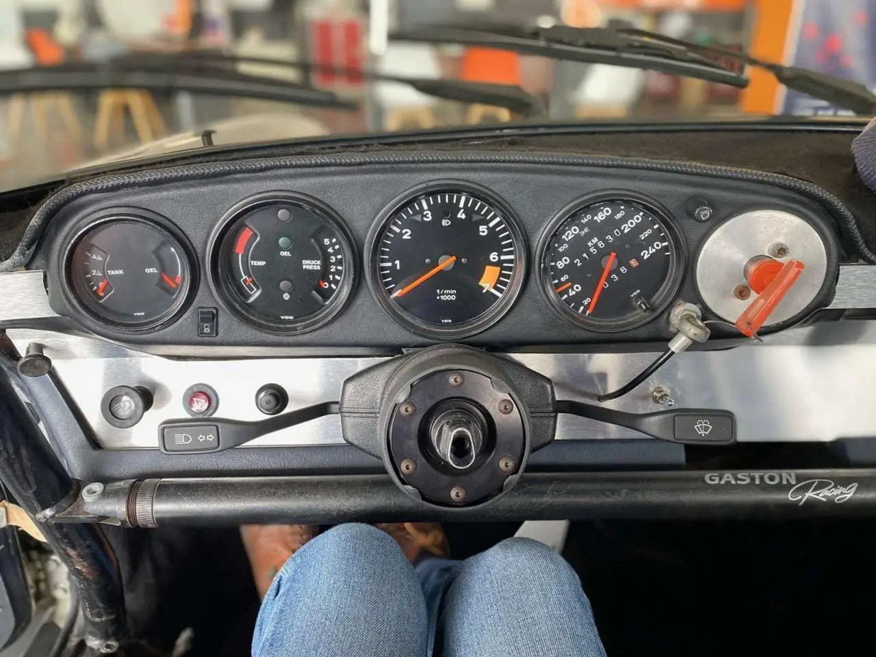 Tableau de bord de Porsche 911 3.0 SC gris, vue frontale centrée sur les compteurs et volant Sparco sans moyeu.